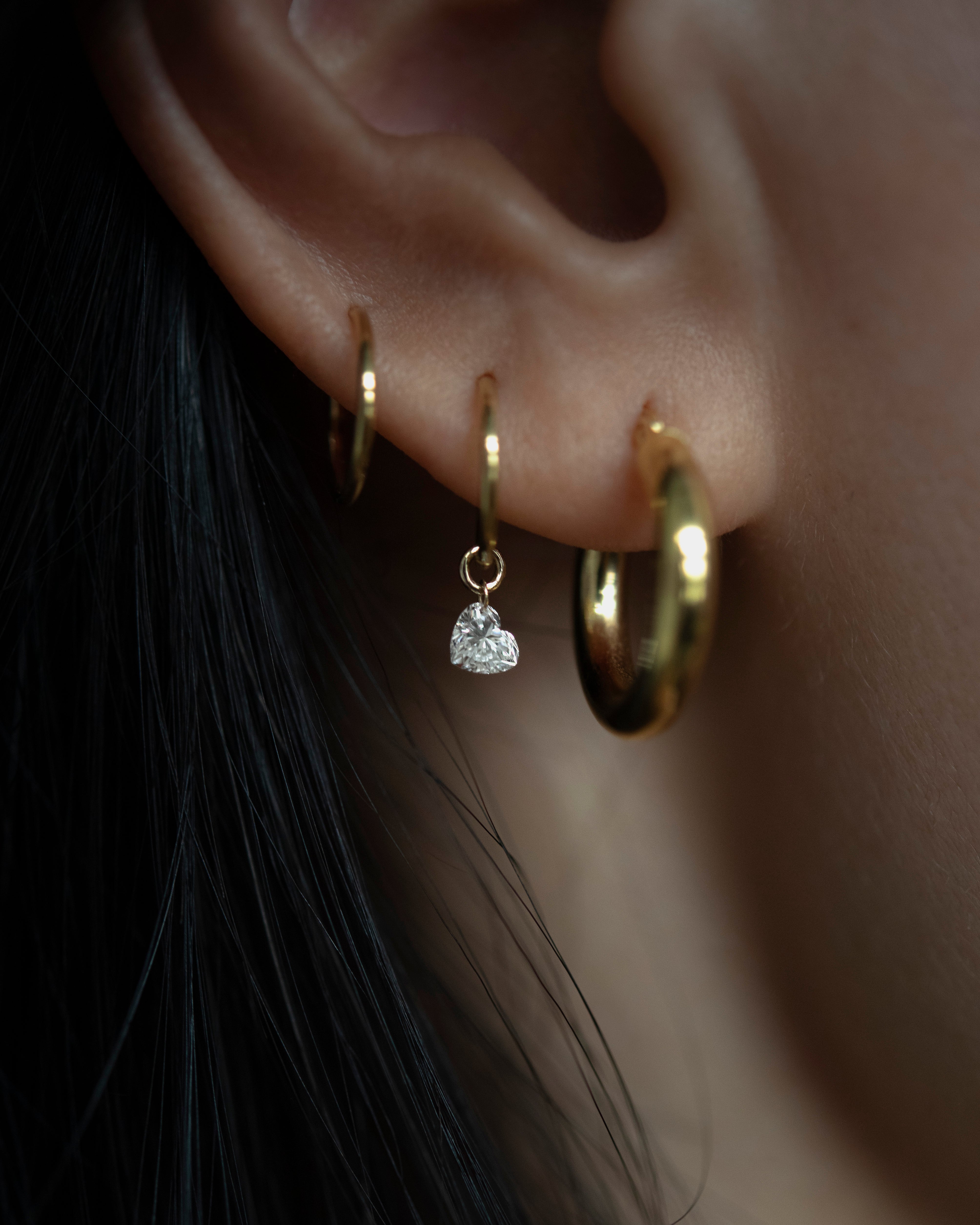 Close-up of an ear wearing gold hoop earrings with a heart-shaped pendant.
